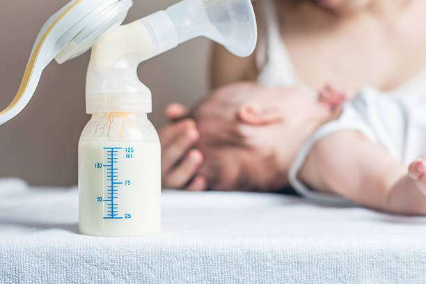 Close-up of a breast pump bottle with milk, mother and baby blurred in background.