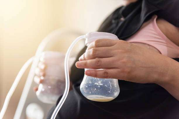 Woman holding breast pump bottle with milk, close-up.