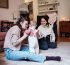 Two moms with a baby. One woman uses a hands-free breast pump in her living room.