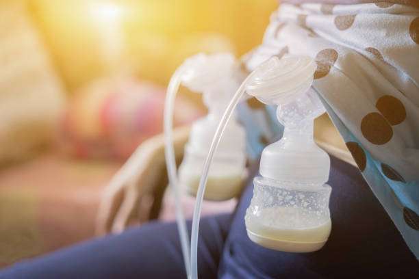 Mother using a double electric breast pump with collected milk. Gentle sunlight in background.