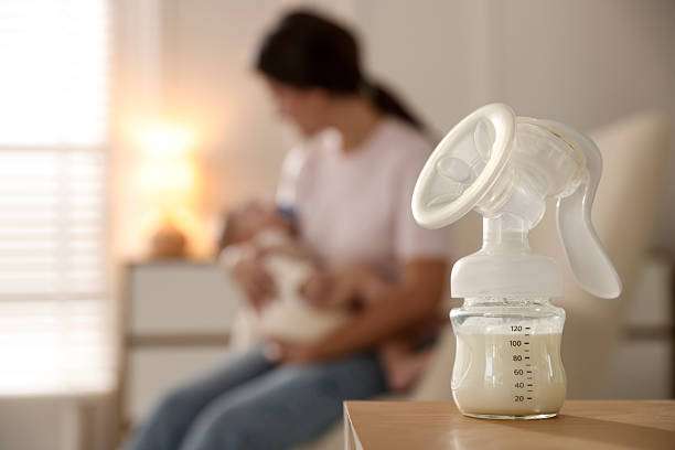 Close-up of breast pump with milk, mother holding baby blurred.