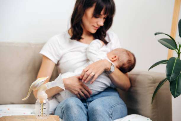 Smiling mother cuddling her baby, with a manual breast pump sitting on the couch.