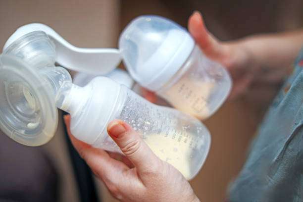 Hands holding a breast pump with collected milk in bottles.