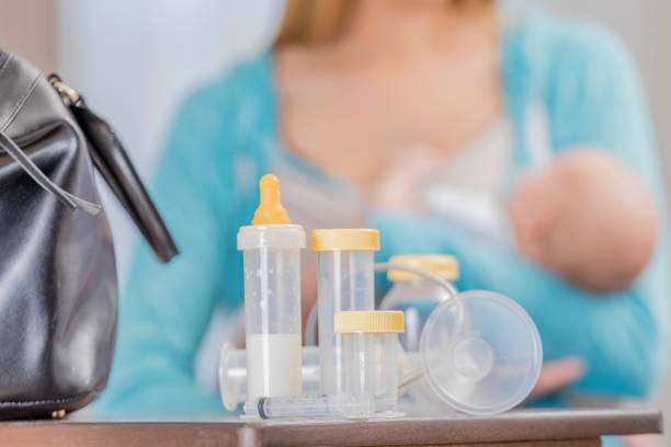 Collection of breast pump parts and milk bottles, woman and baby in background.