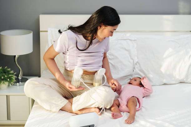 Mother using breast pump with baby on bed.