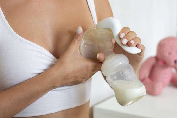 Close-up of a woman's hands using a manual breast pump to express milk.