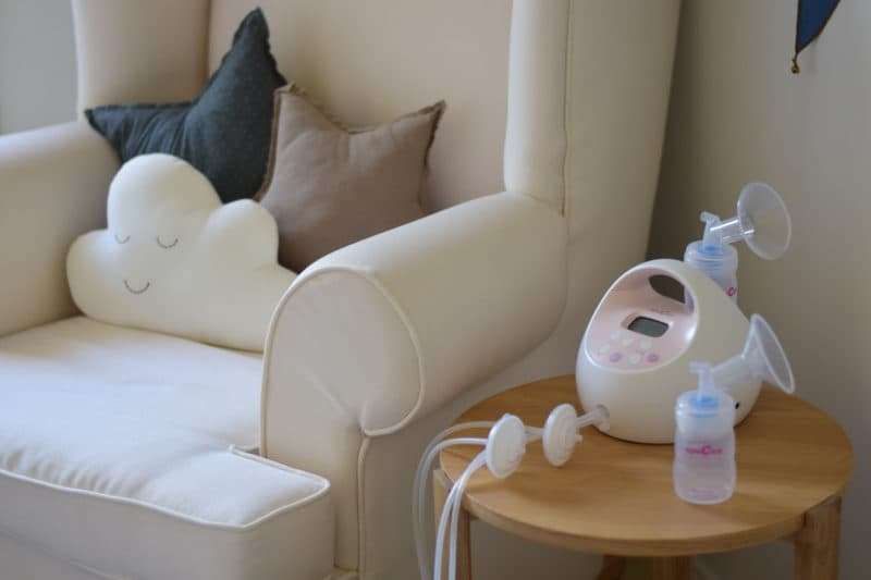 White breast pump with bottles sits on wooden table next to chair.